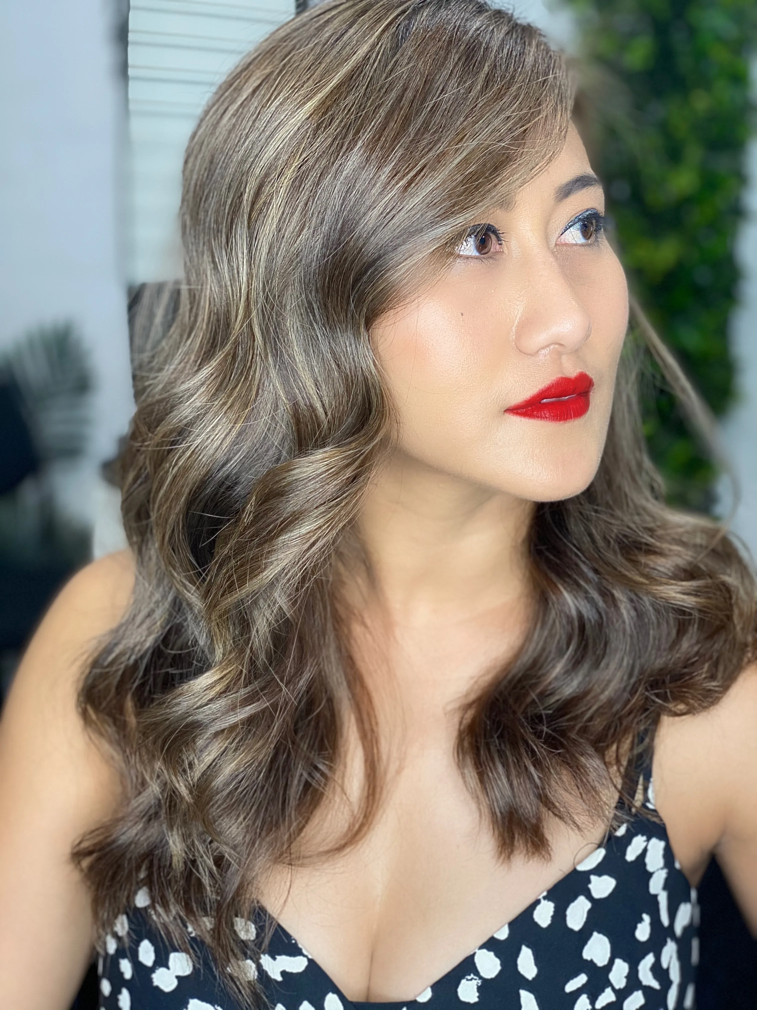 Bronde highlighted waves with bold red lip, green moss wall behind